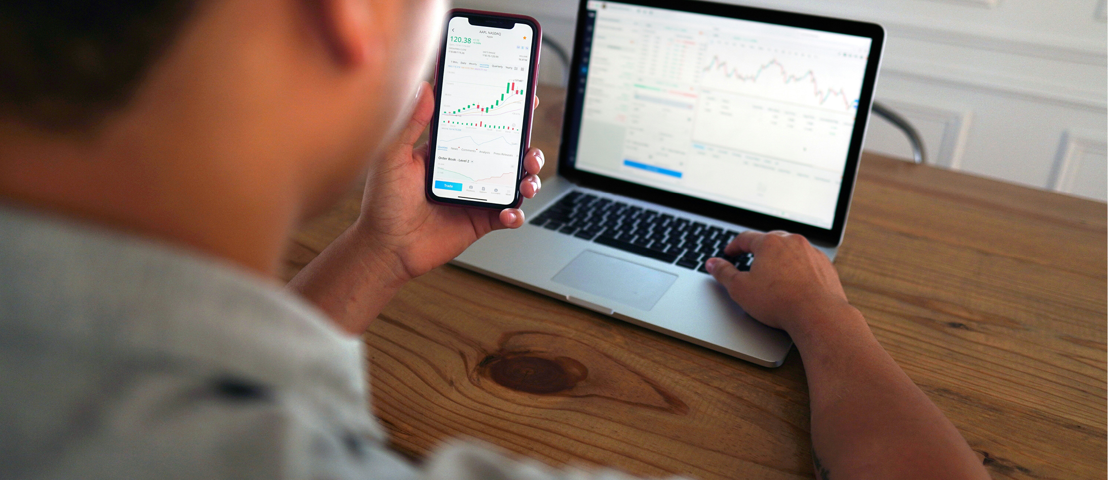 Man sitting at a desk using cell phone and computer to do investments